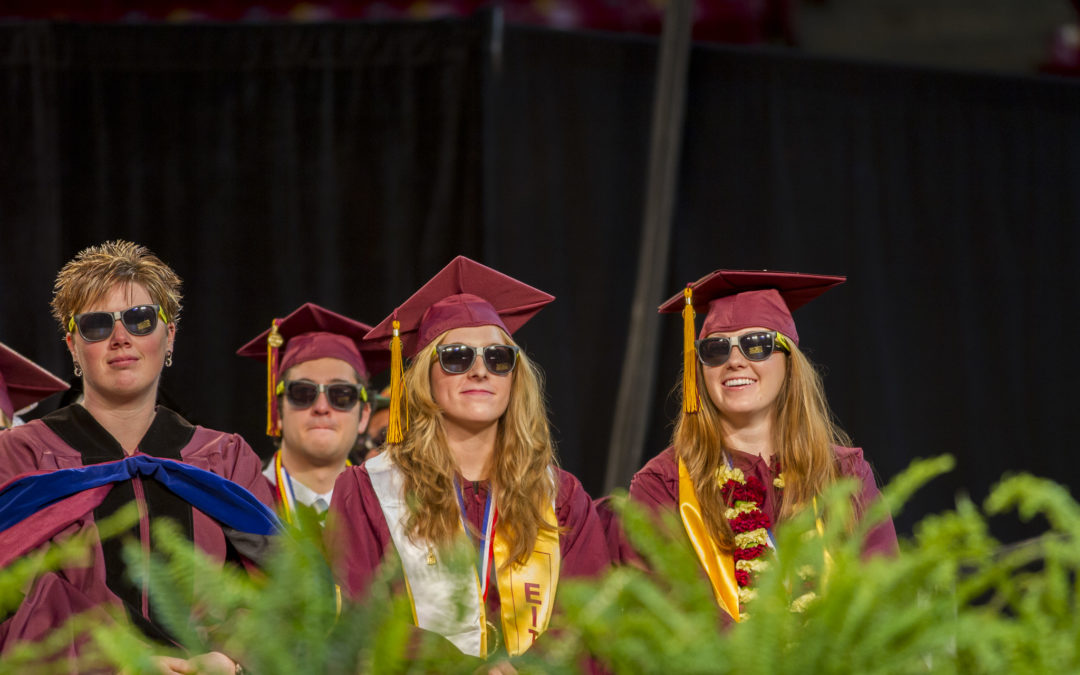 Four graduates sit on stage in full regalia -- and sunglasses!