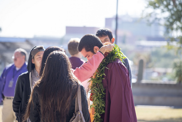 A graduate's monther places a floral lei around her son's neck before graduation
