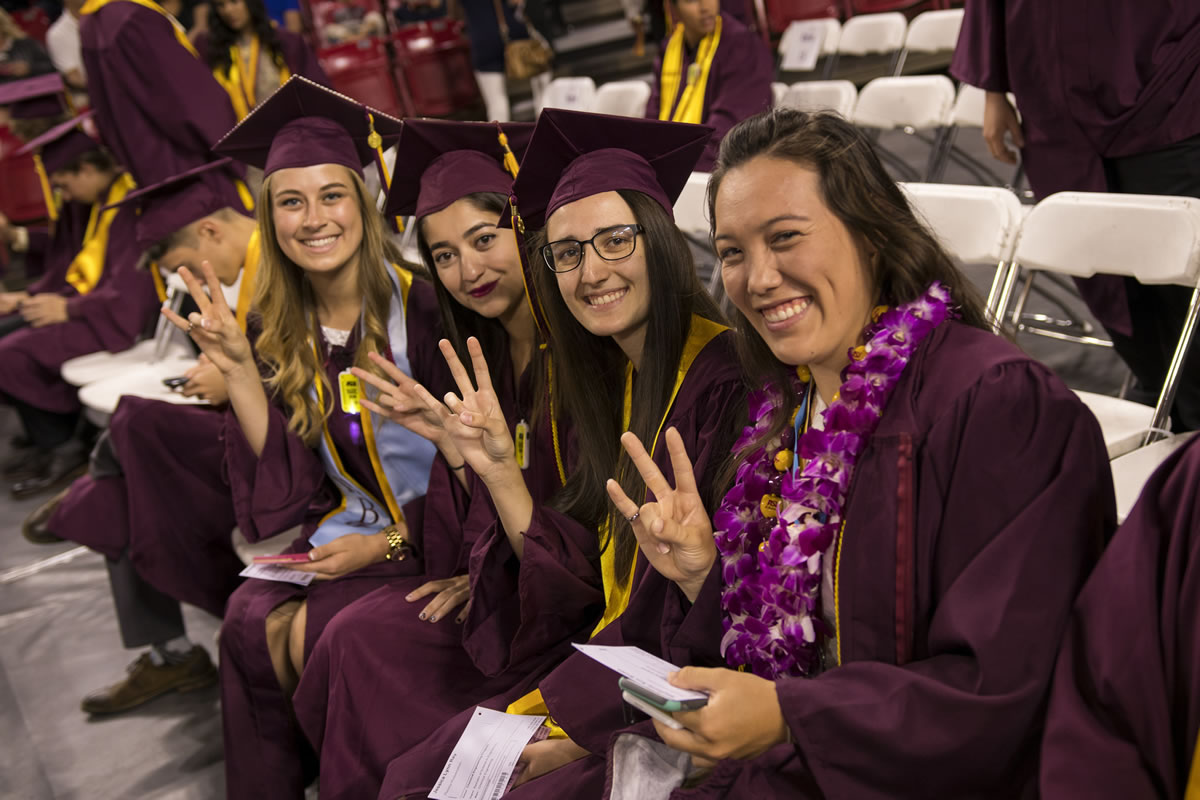 a group of four young women graduates make the pitchfork symbol with their hands at graduation
