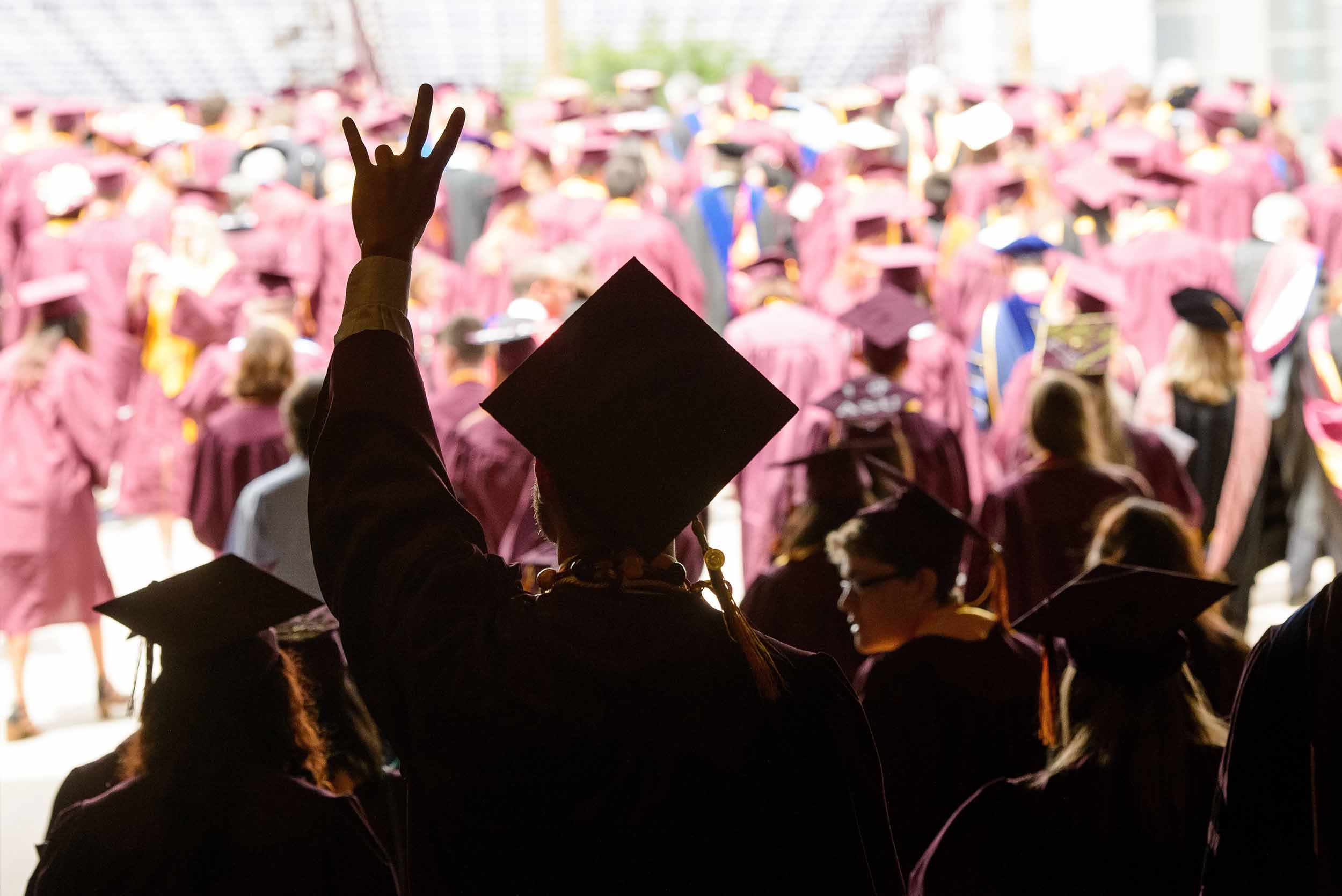 A graduate makes the ASU pitchfork gesture in a crowd of graduates