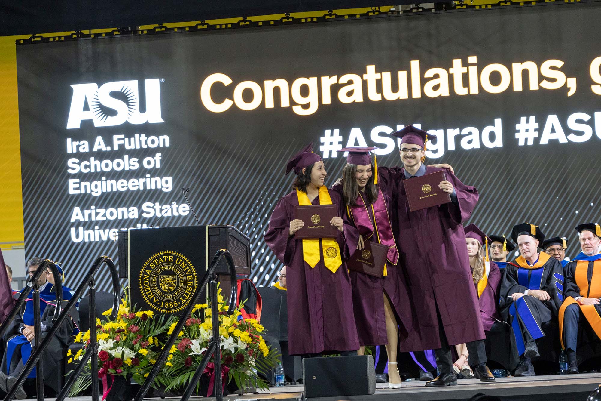 Three graduates stand together on the stage at the ASU Engineering Convocation ceremony