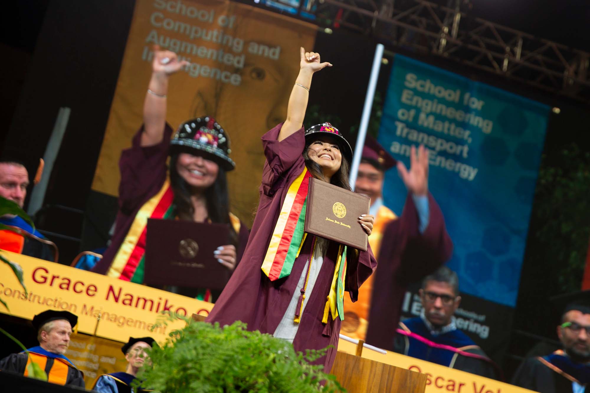 An undergraduate student smiles broadly and raises her hand in the air, holding her diploma in the other, crossing the stage at the ASU Engineering Fall 2023 Undergraduate Convocation