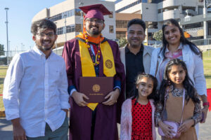 A graduate stands with his family, including siblings, parents and young children.