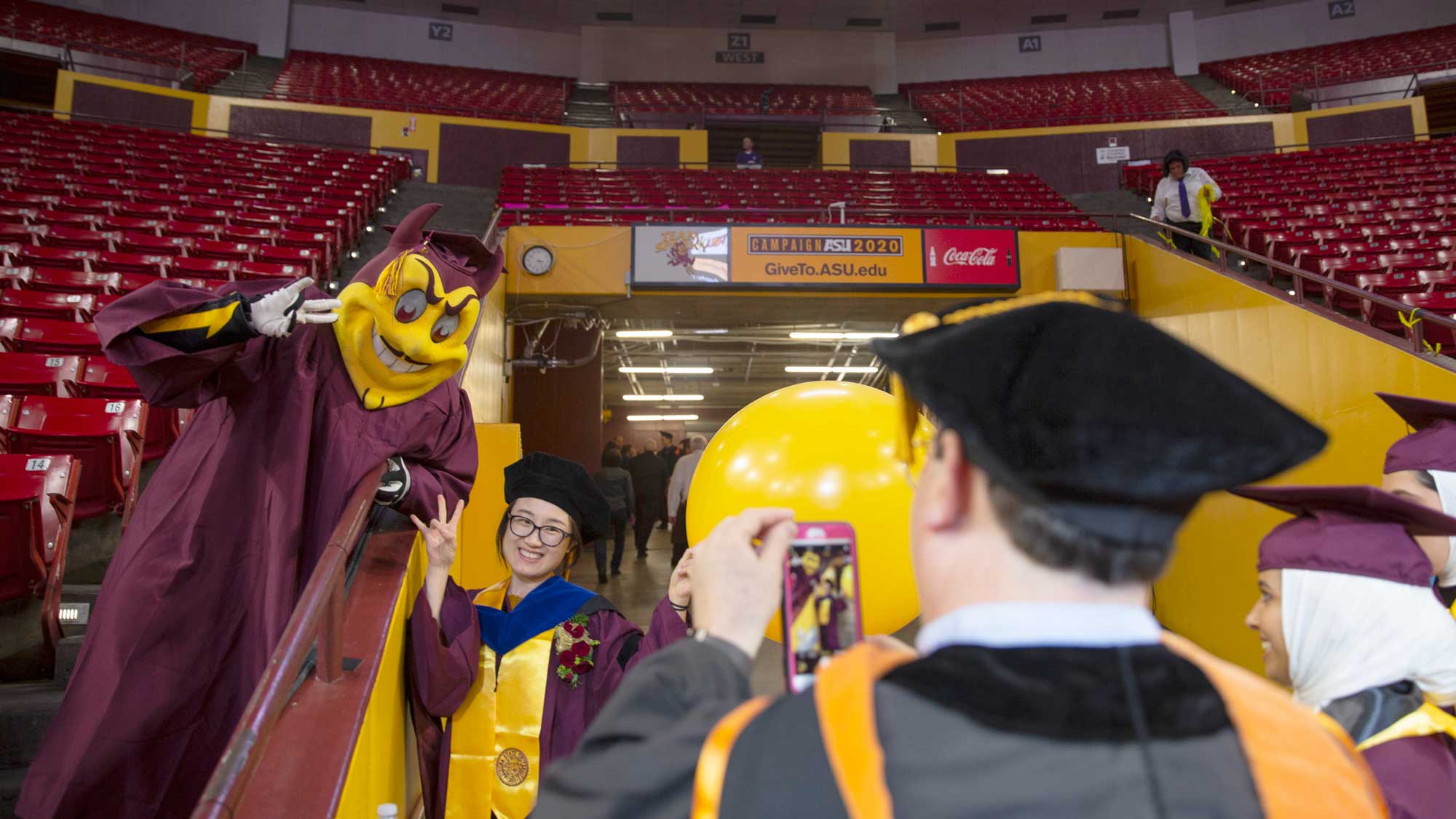 ASU's mascot, Sparky, in graduation regalia, poses for a photo with a graduating student at the ASU Engineering Convocation