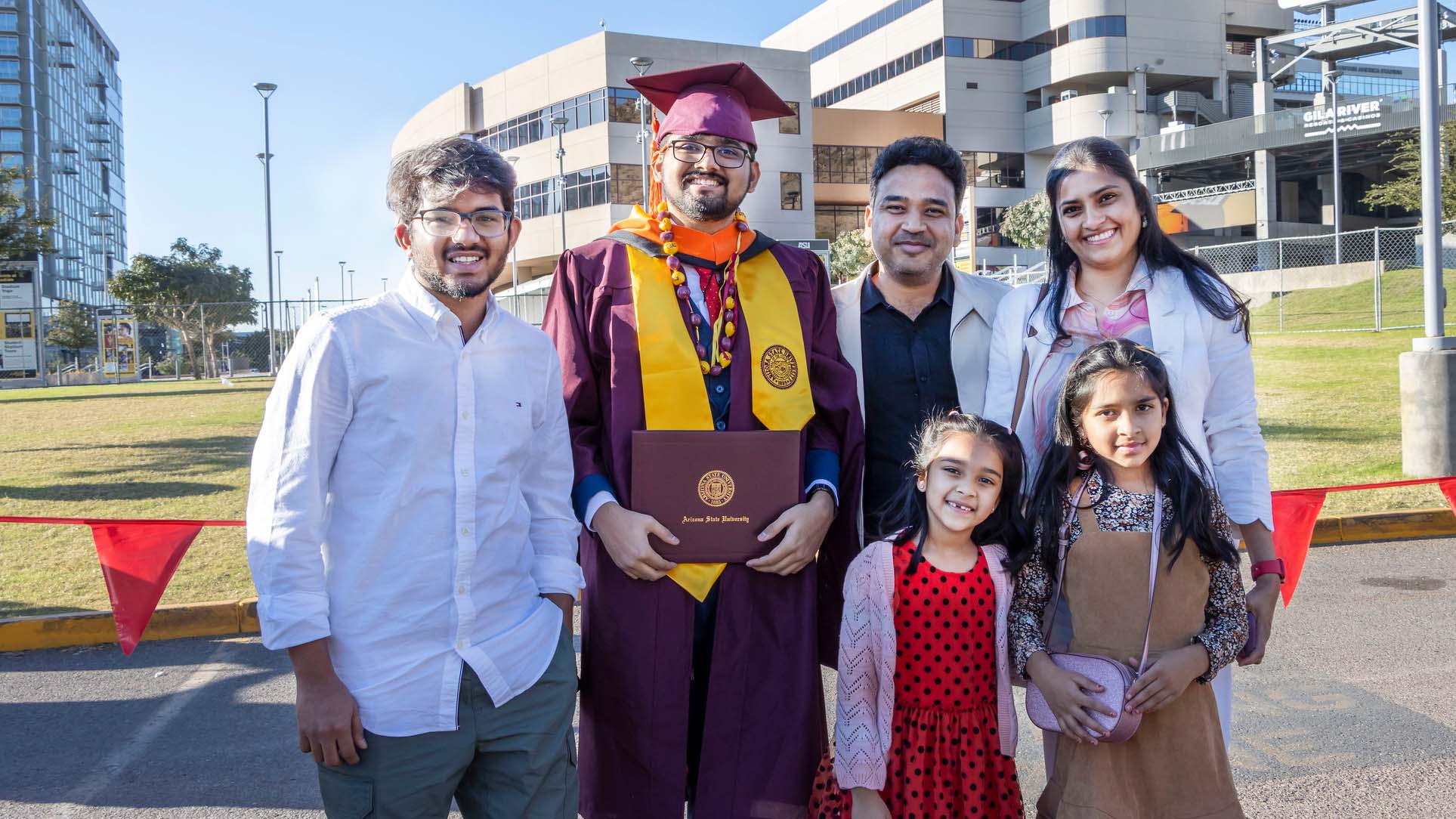 A graduate stands with his family, including siblings, parents and young children.