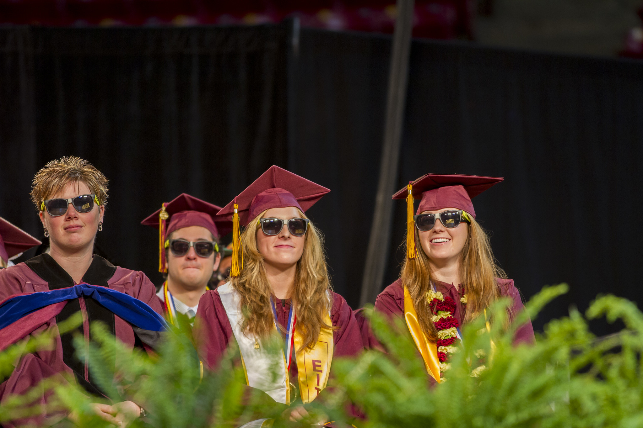 Four graduates sit on stage in full regalia -- and sunglasses!