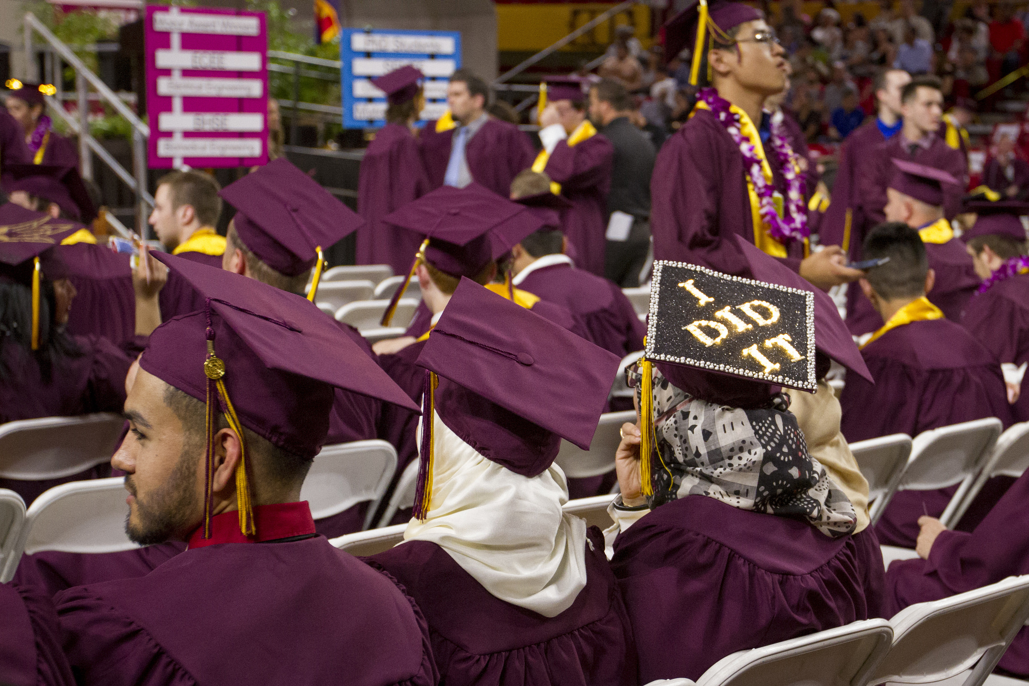 This image shows a group of seated graduates at a convocation ceremony, dressed in maroon caps and gowns.