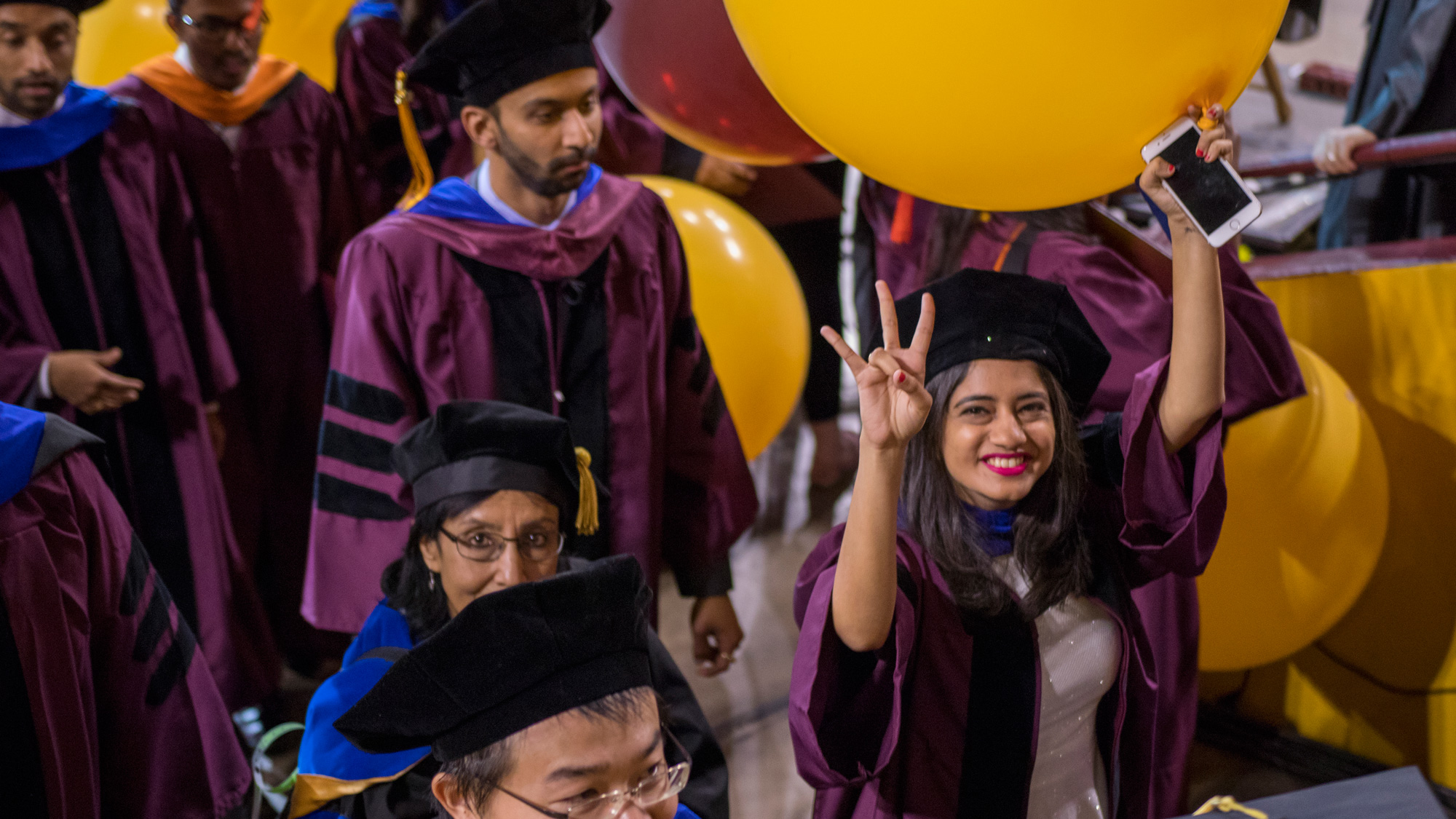 A student holds a balloon in one hand and holds an ASU pitchfork gesture in the other, as she smiles leaving Convocation