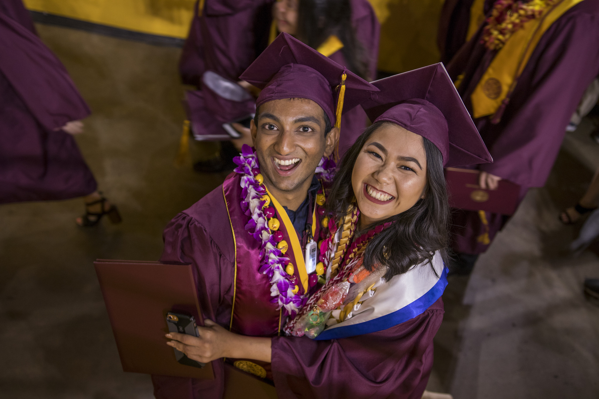 Two graduates, a man and woman, embracing, smile excitedly after the convocation ceremony