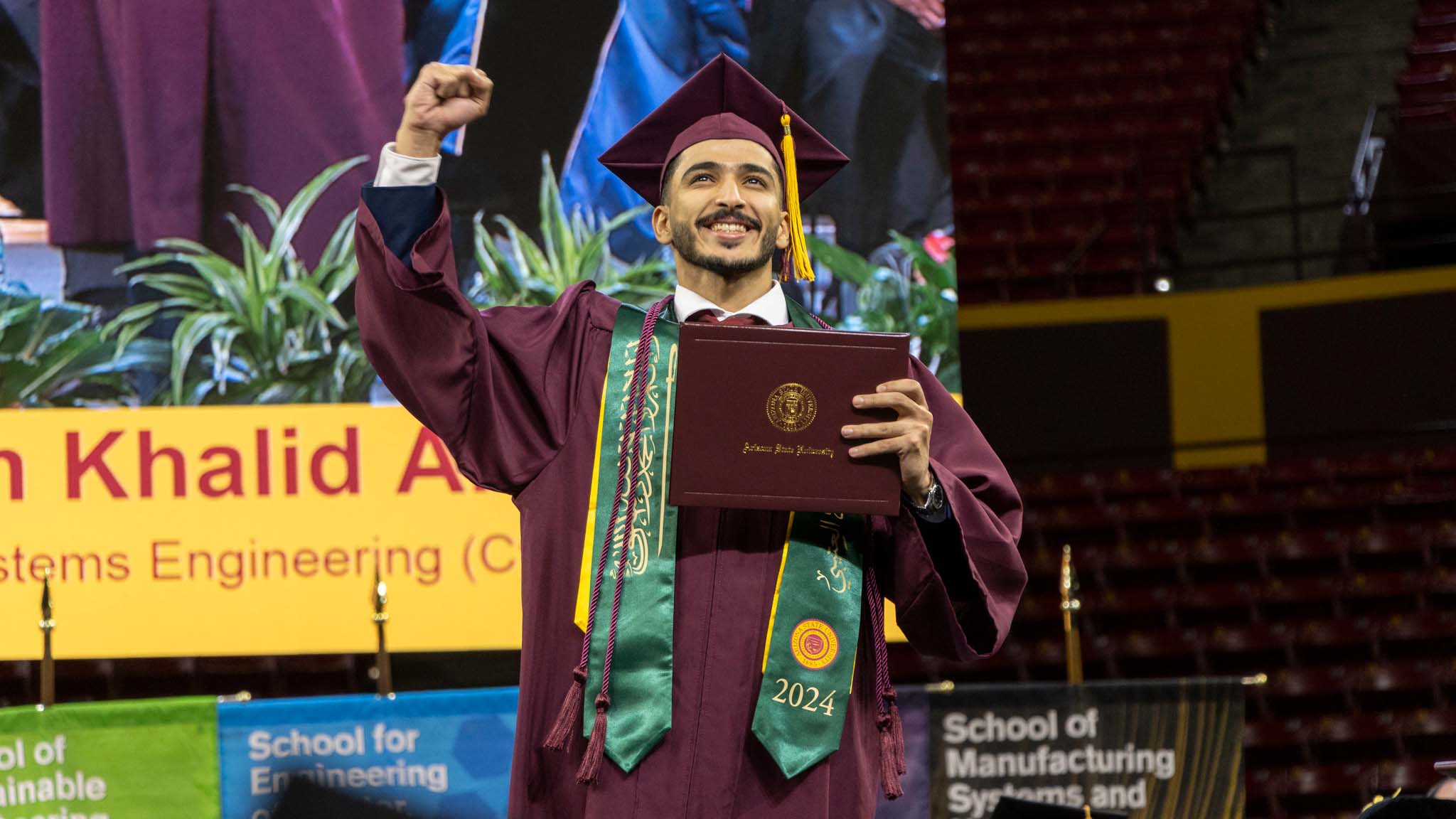 A man proudly holds his diploma while wearing a maroon graduation gown, symbolizing his academic achievement.