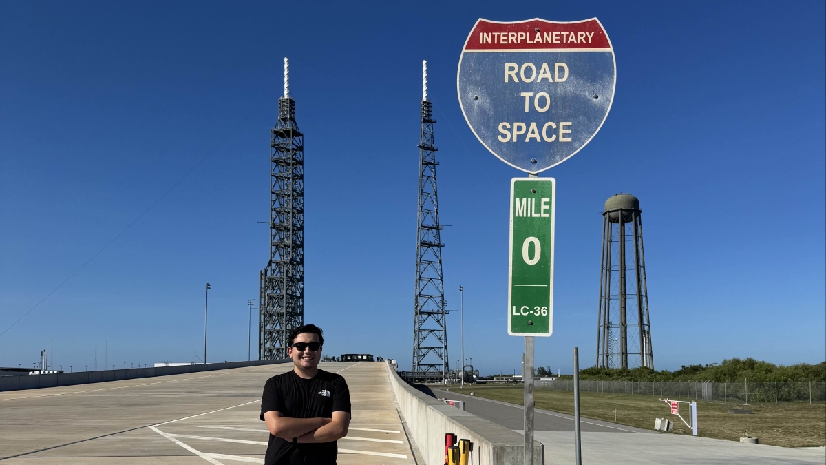 Luke Wybourn stands in front of a space vehicle launchpad.