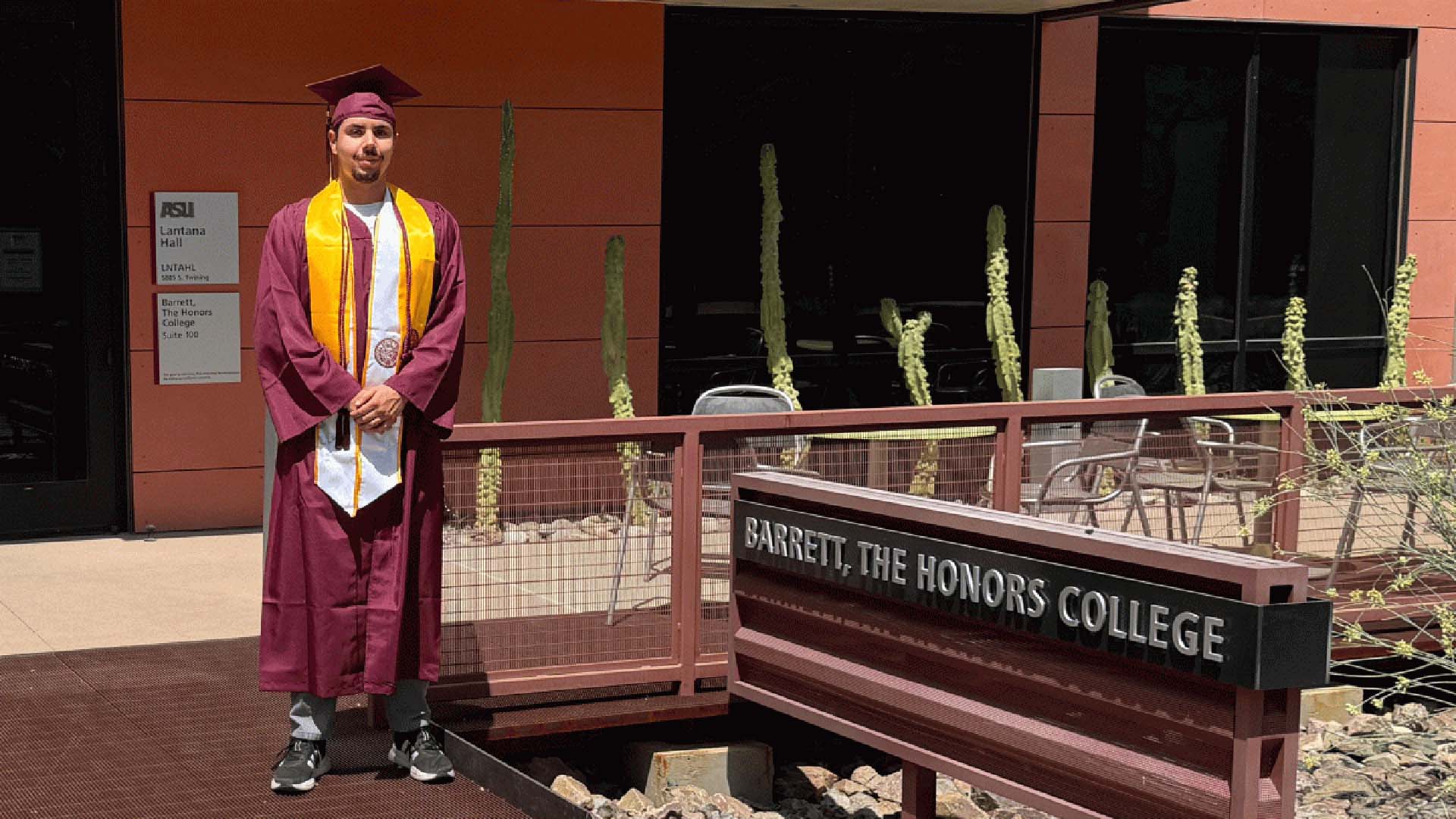 Graduate in cap and gown stands outside Barrett, The Honors College building.